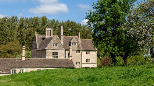 Lyveden's manor house, nestled behind a grassy hill and surrounded by lush green trees in springtime.